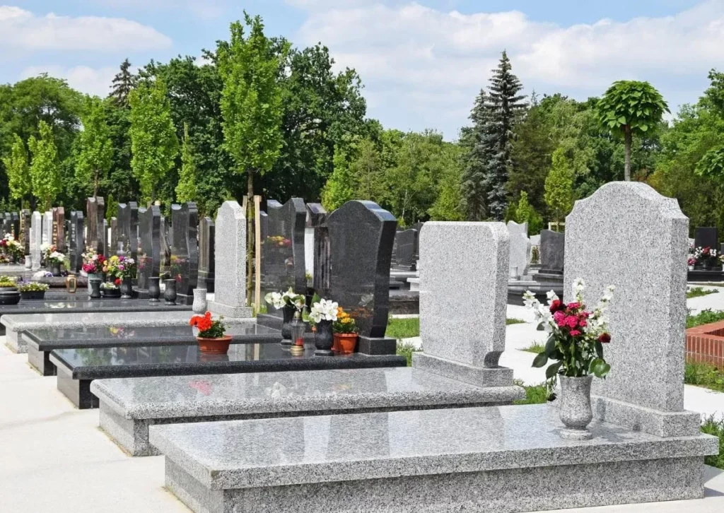 Alignement de monuments funéraires et sépultures en granit dans un cimetière paysagé.